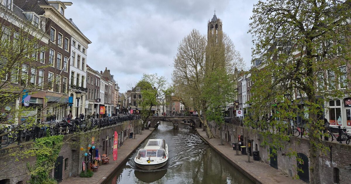A tour boat on the Oudegracht in Utrecht, with the wharves and cellars at water level, old houses, spring trees and the Dom Tower at the end of the canal