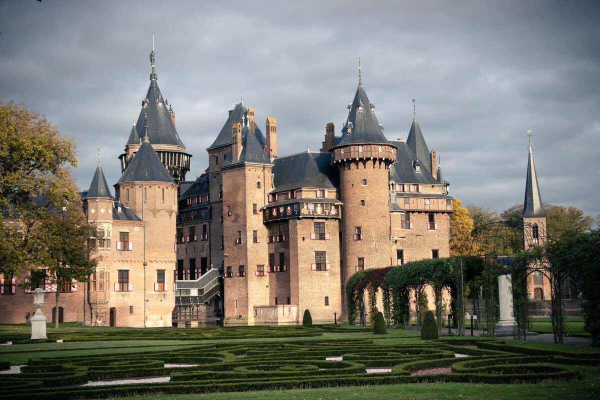 The red brick towers and pointed slate roofs of Castle De Haar above its formal gardens, under a gray autumn sky