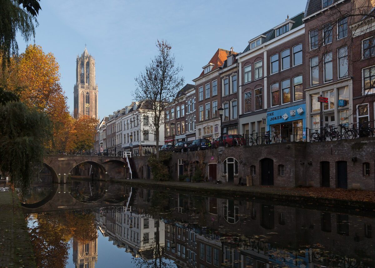 The Oudegracht canal in autumn, with the stone wharves at water level, old houses above and the Dom Tower reflected in the still water
