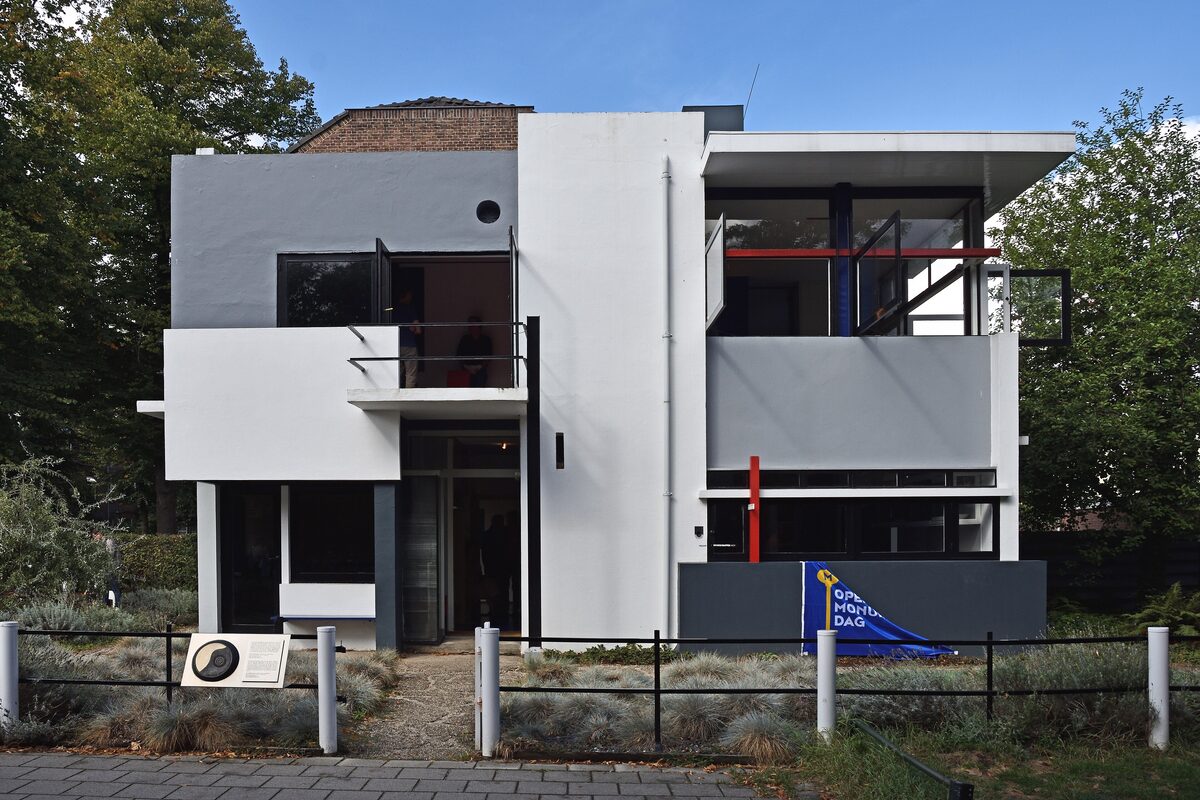 The Rietveld Schröder House, a white and gray box of flat planes and balconies with red, yellow and blue lines, behind a low fence
