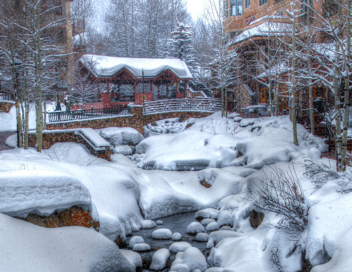 Snow piled on the rocks of a creek beside lodges and bare aspens in Beaver Creek Village