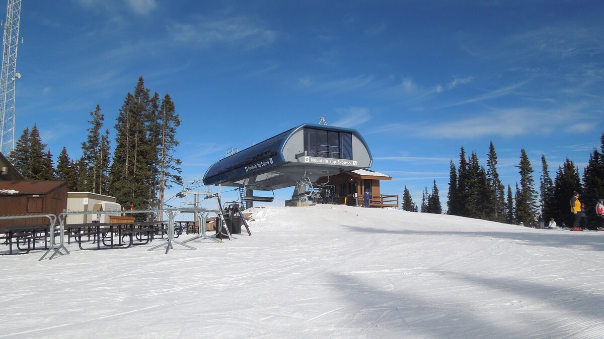 The top station of the Mountaintop Express chairlift on Vail Mountain, with a groomed slope in sunshine and spruce trees behind