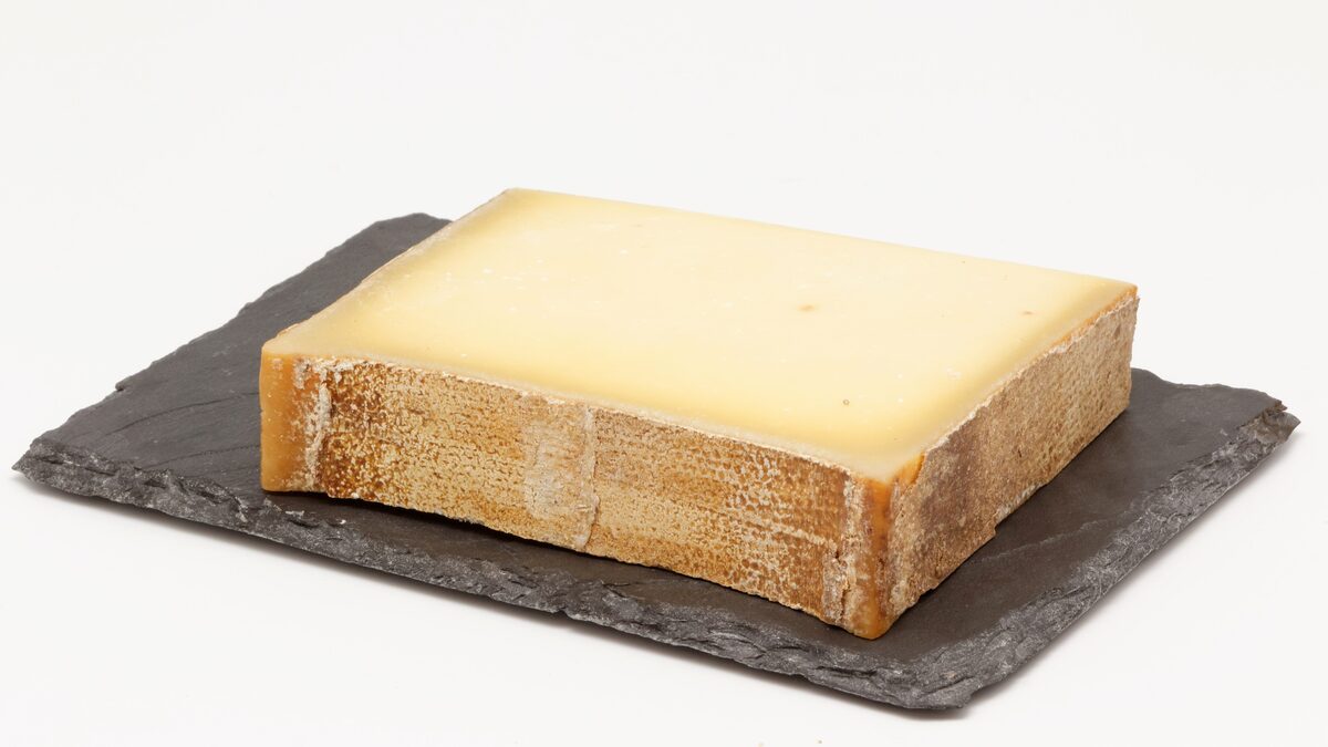 A block of Beaufort cheese with a pale yellow interior and a darker rind edge, on a slate board