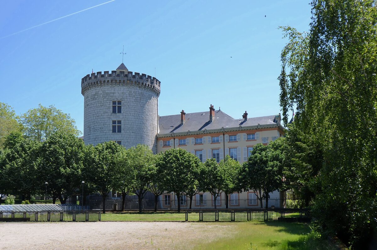 The round stone tower of the Château des Ducs de Savoie in Chambéry, above a lawn and trees