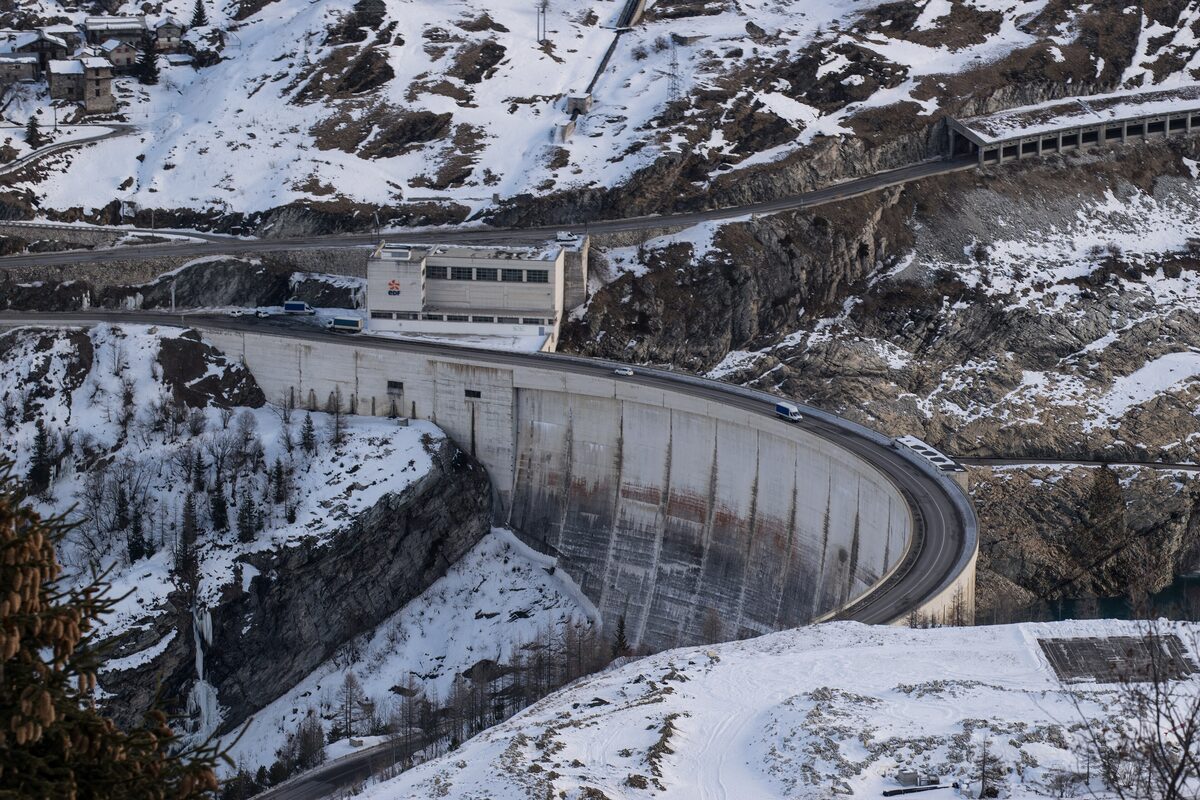 The curved concrete Tignes dam with snow on the slopes around it and a road running along the reservoir