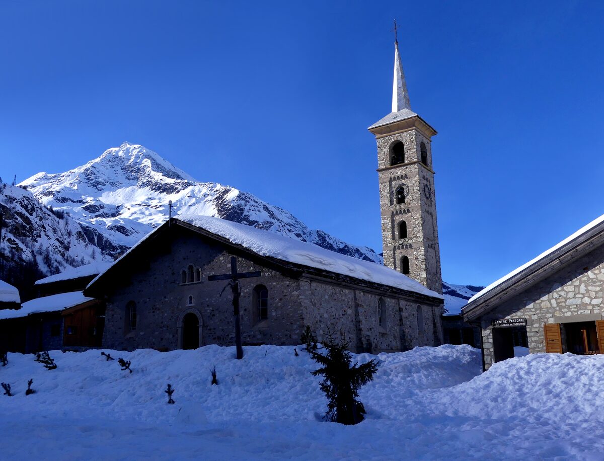 The stone church of Saint-Jacques with its tall bell tower in the snow at Tignes 1800