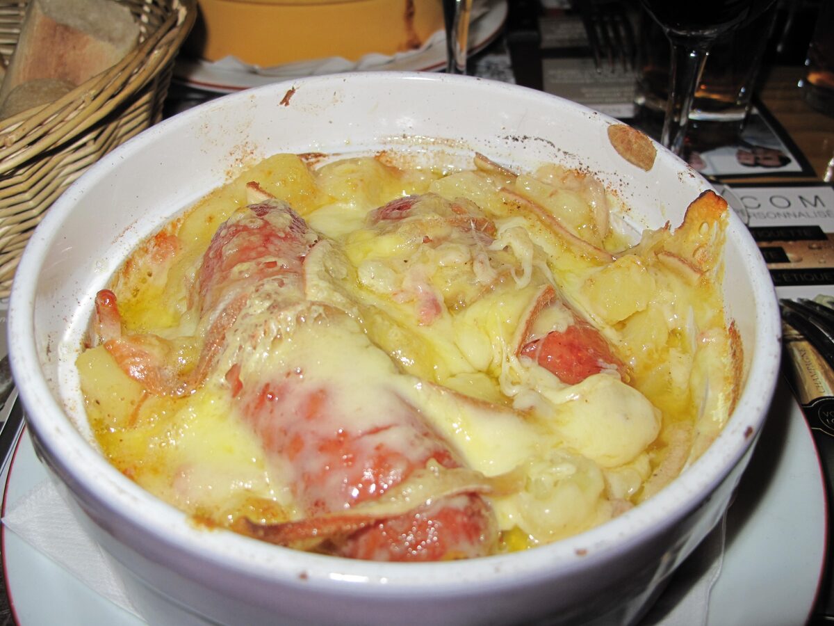 Diots sausages baked with potatoes under melted cheese in a white gratin dish