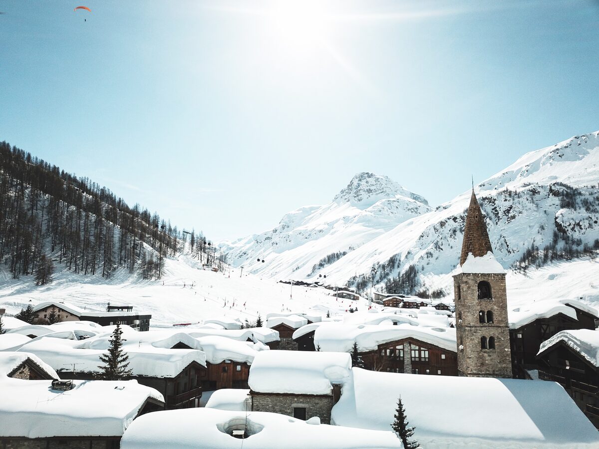 The old village of Val d'Isère under deep snow, with the stone bell tower of the church and ski slopes rising behind the roofs