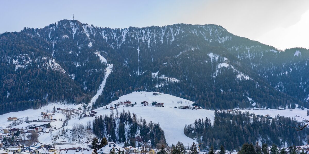 Sureghes, a hamlet of Ortisei, under snow with a ski slope running up the mountain behind