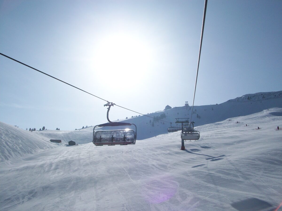 A chairlift and a wide snowy piste on the Saslong run, with the sun flaring over the lift