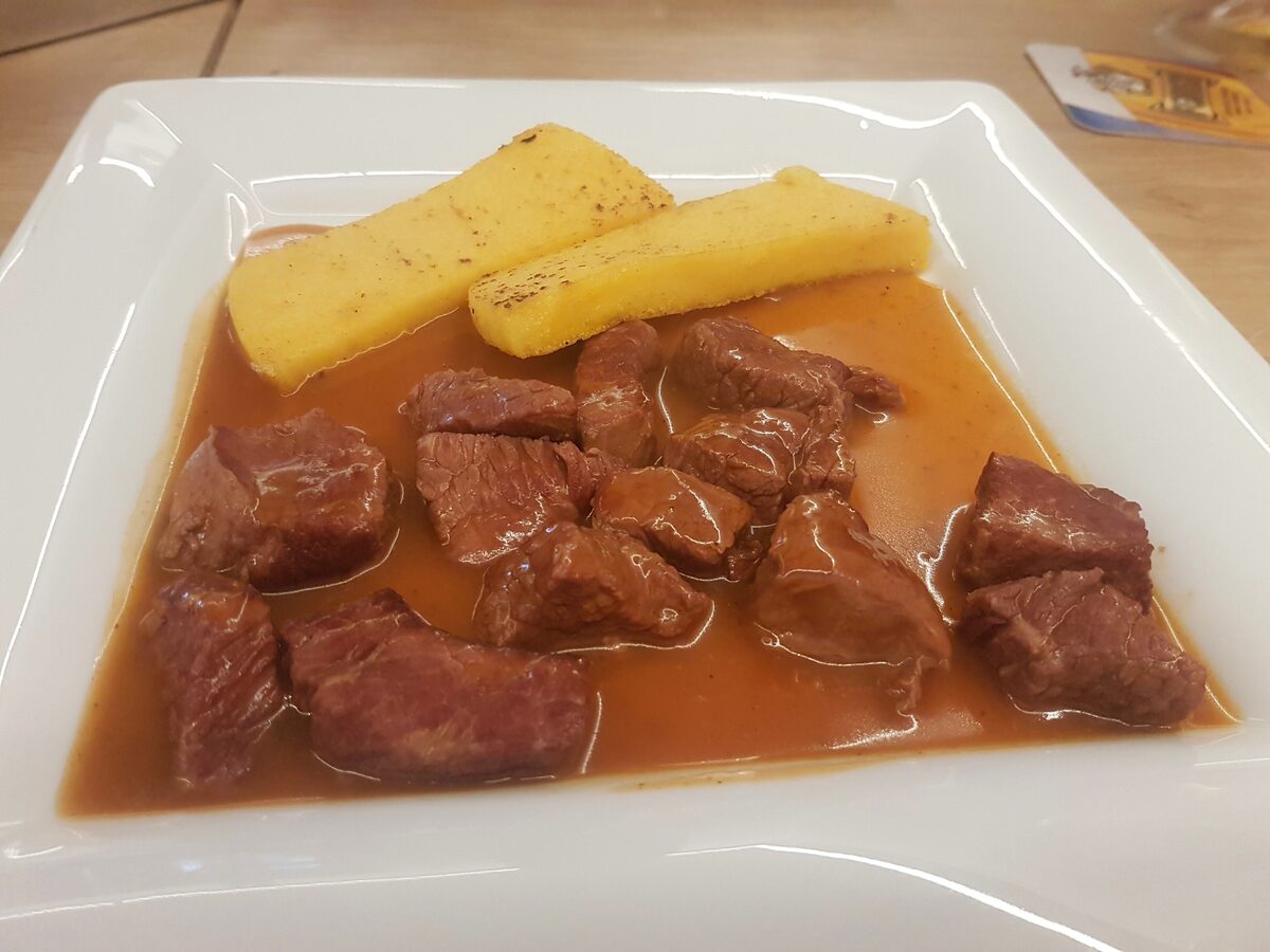 Beef goulash in a dark sauce with two roasted slices of polenta on a square white plate