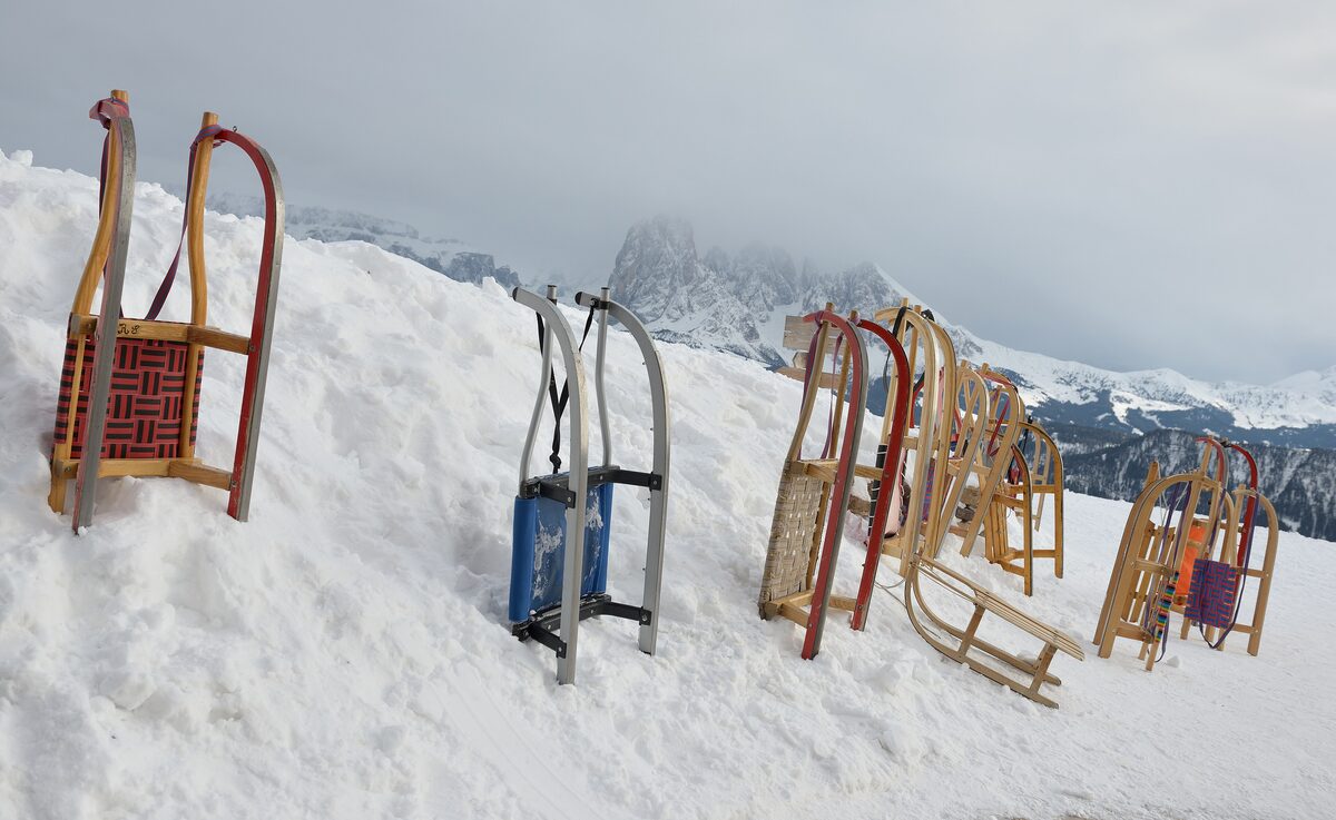 Wooden toboggans stuck upright in the snow on Resciesa, with the Sassolungo faint in the clouds behind
