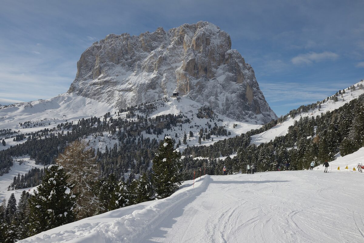 The Sassolungo (Langkofel) rising above a groomed piste and snowy pine forest on the Val Gardena side