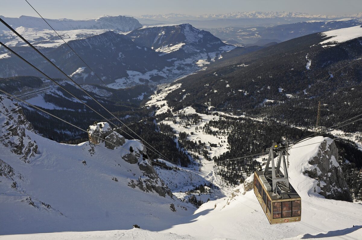 The cable car to Seceda above snowy slopes, with the valley and its forests falling away below