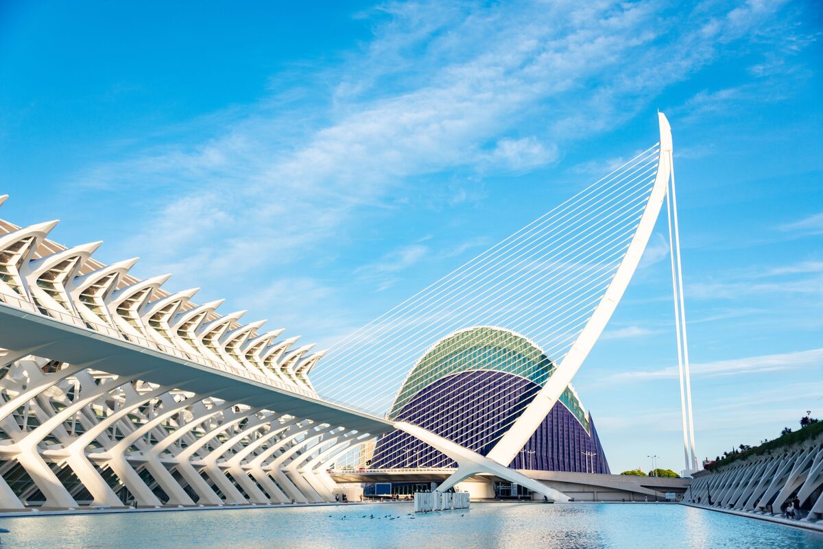 The white ribbed walkway of the Museu de les Ciències and the blue-and-white Àgora beside a pool, with a white cable bridge above