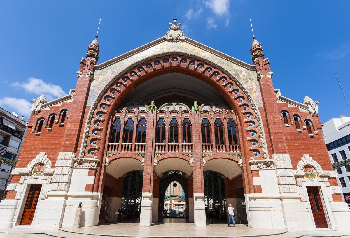 The red brick and tiled Modernist arch of the Mercado de Colón in Valencia against a blue sky