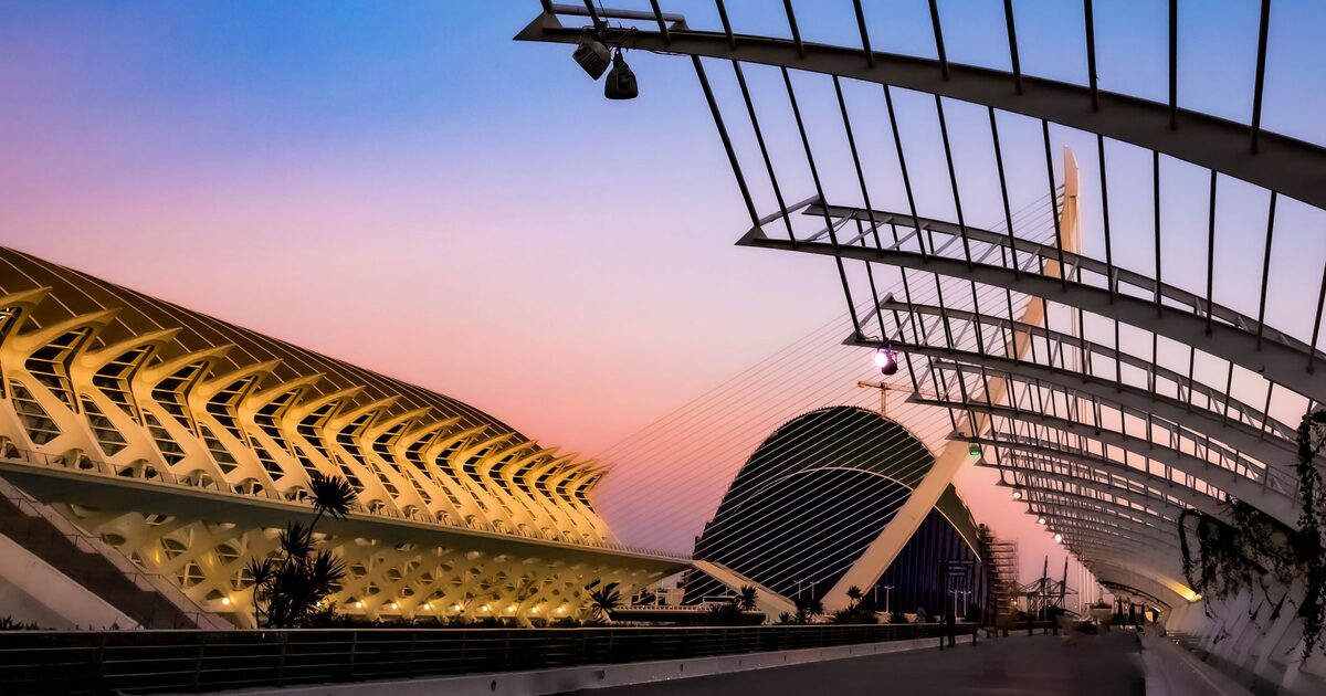 The white ribbed arches of the City of Arts and Sciences and the dome of the Hemisfèric lit up at sunset under a pink and blue sky