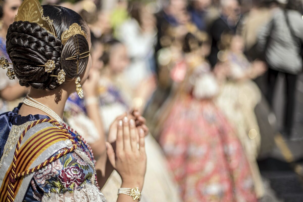 A Fallera in traditional Valencian dress and braided hair with gold combs, praying, at a Fallas procession