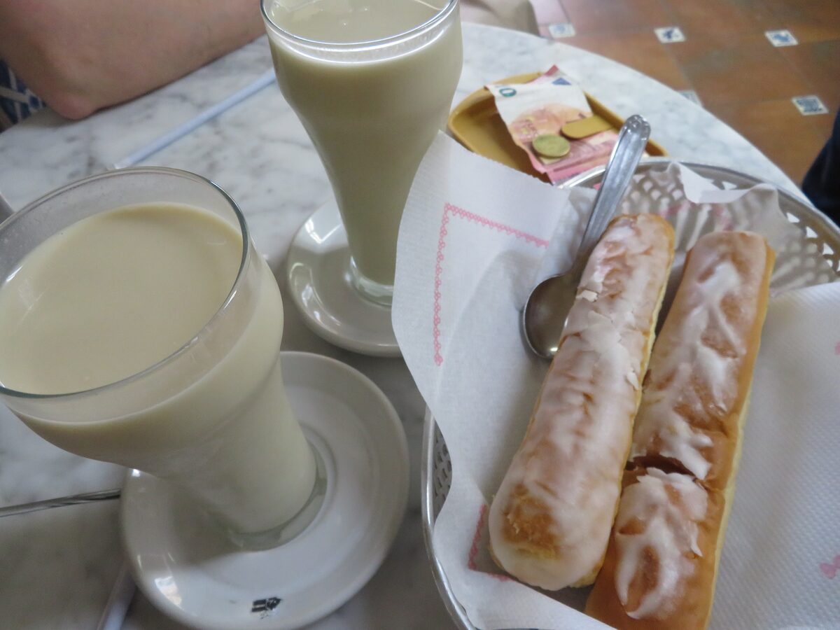 A glass of horchata next to sugar-glazed fartons on a café table