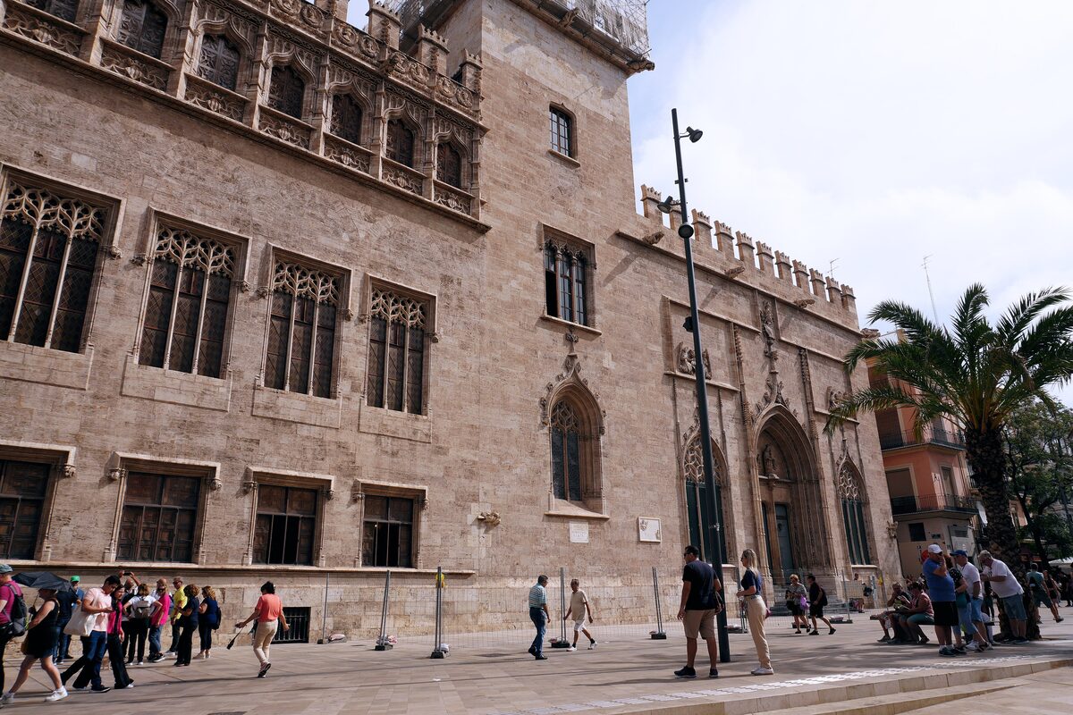 The late Gothic facade of the Lonja de la Seda in Valencia, with its crenellated roofline and arched doorway, and palm trees in front