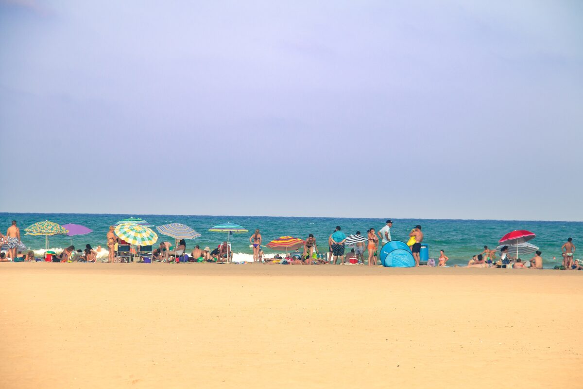 Malvarrosa beach in Valencia, a wide stretch of golden sand with colorful umbrellas and swimmers along the edge of the sea