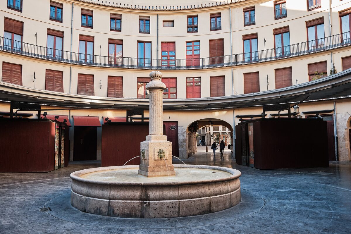 The round Plaza Redonda in Valencia, a circular courtyard of white and red buildings with a stone fountain in the middle