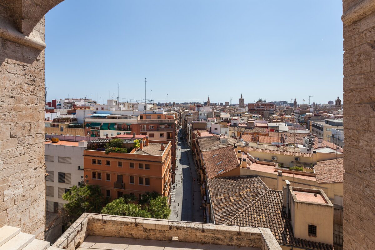View from the Torres de Quart down a long, straight street of old buildings and rooftops, framed by the tower's stone walls