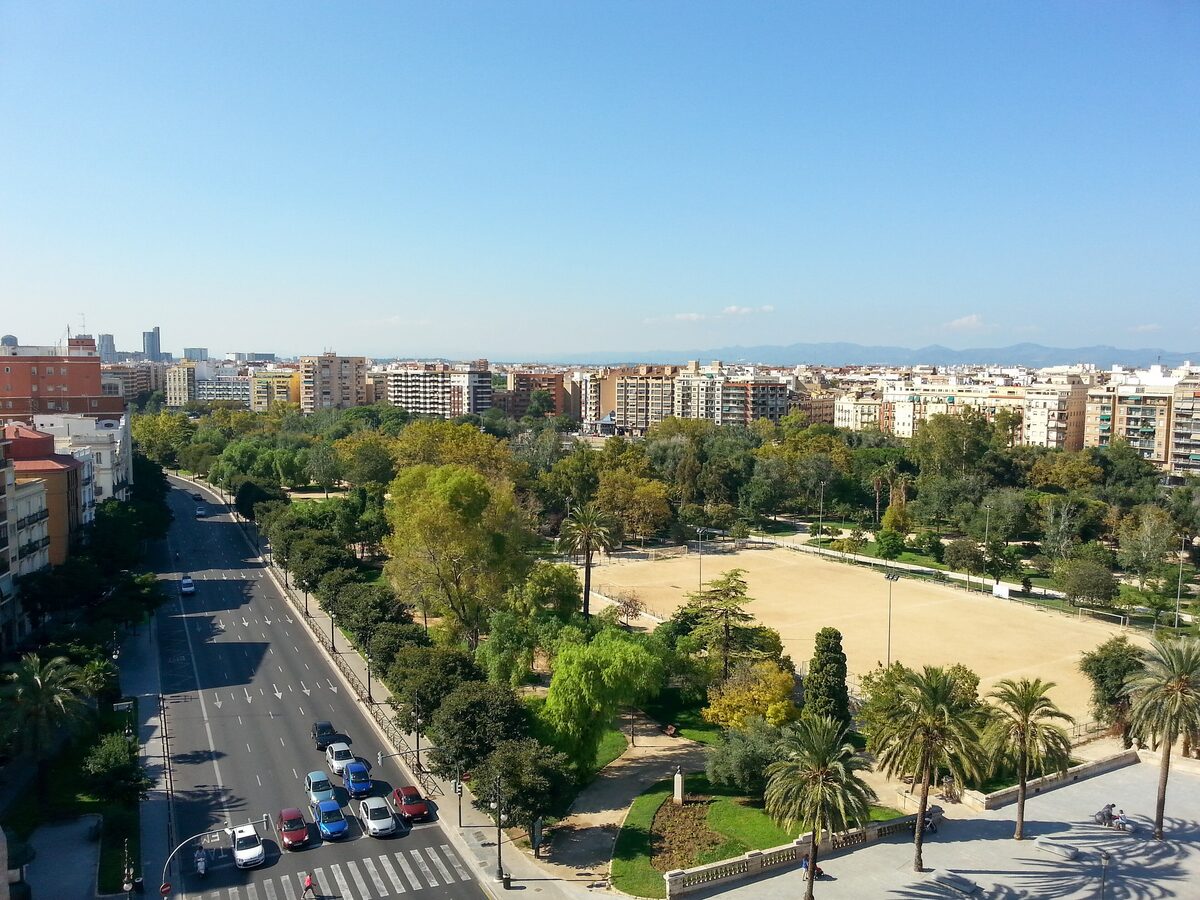 View from above of the green Turia gardens running through Valencia, with trees, paths and a sports field beside a city avenue