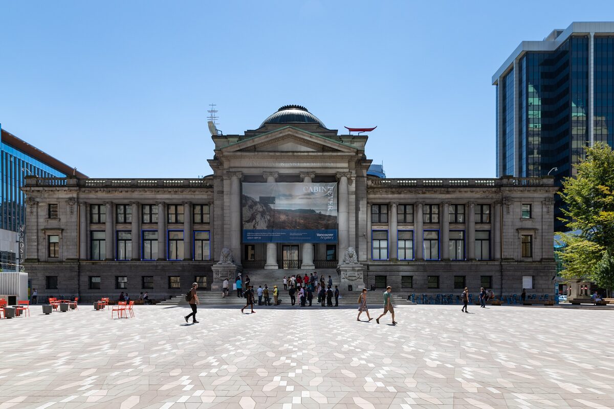 The neoclassical facade of the Vancouver Art Gallery facing Robson Square, with people crossing the plaza