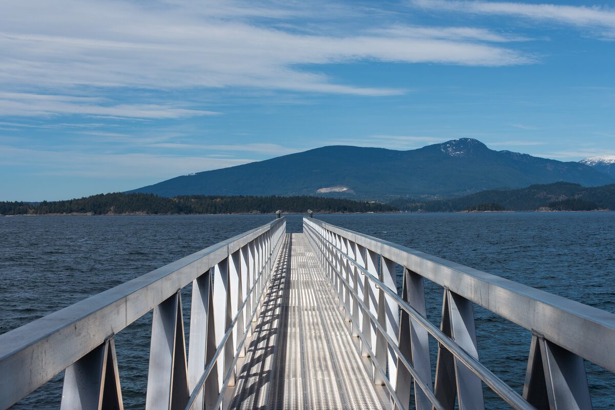 A long aluminum dock running out over the water at Bowen Bay on Bowen Island, with a forested mountain across Howe Sound