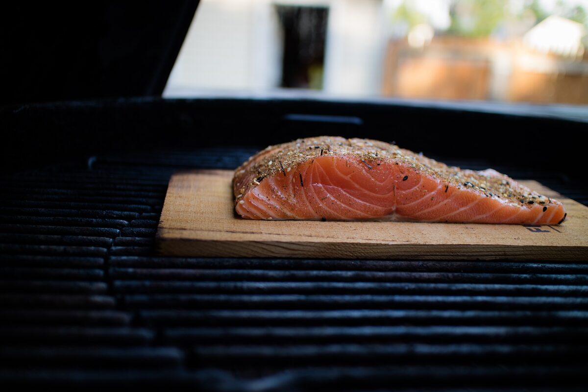 A seasoned salmon fillet cooking on a cedar plank on a barbecue grill