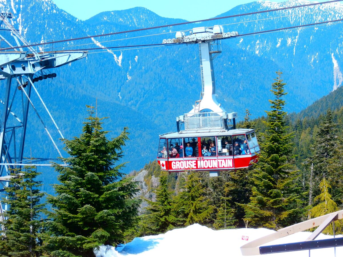 A red Grouse Mountain Skyride gondola cabin full of passengers on its cable above evergreen trees and mountain slopes