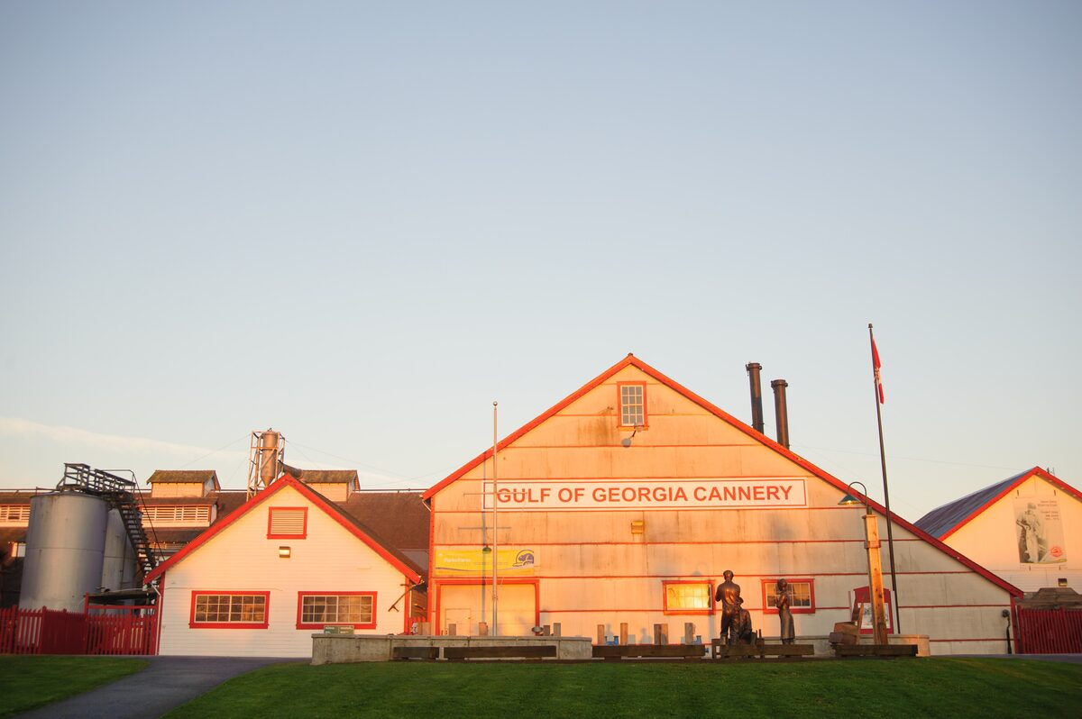 The red-trimmed wooden buildings of the Gulf of Georgia Cannery in warm evening light, with the name on the gable