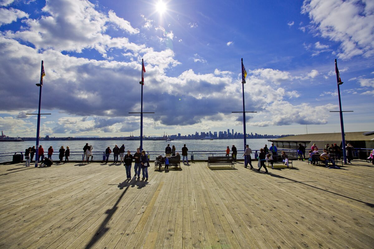 The wooden pier at Lonsdale Quay with visitors at the rail and the Vancouver skyline across the water