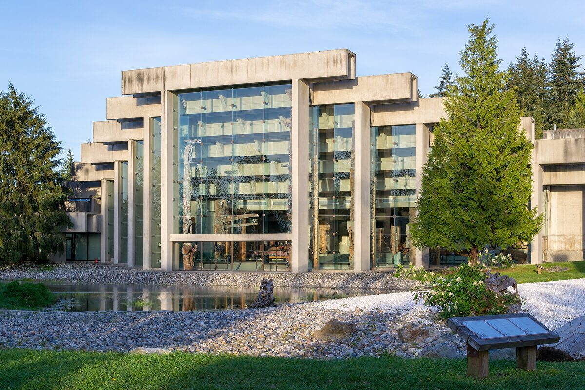 The concrete and glass front of the Museum of Anthropology at UBC, with trees and a reflecting pond