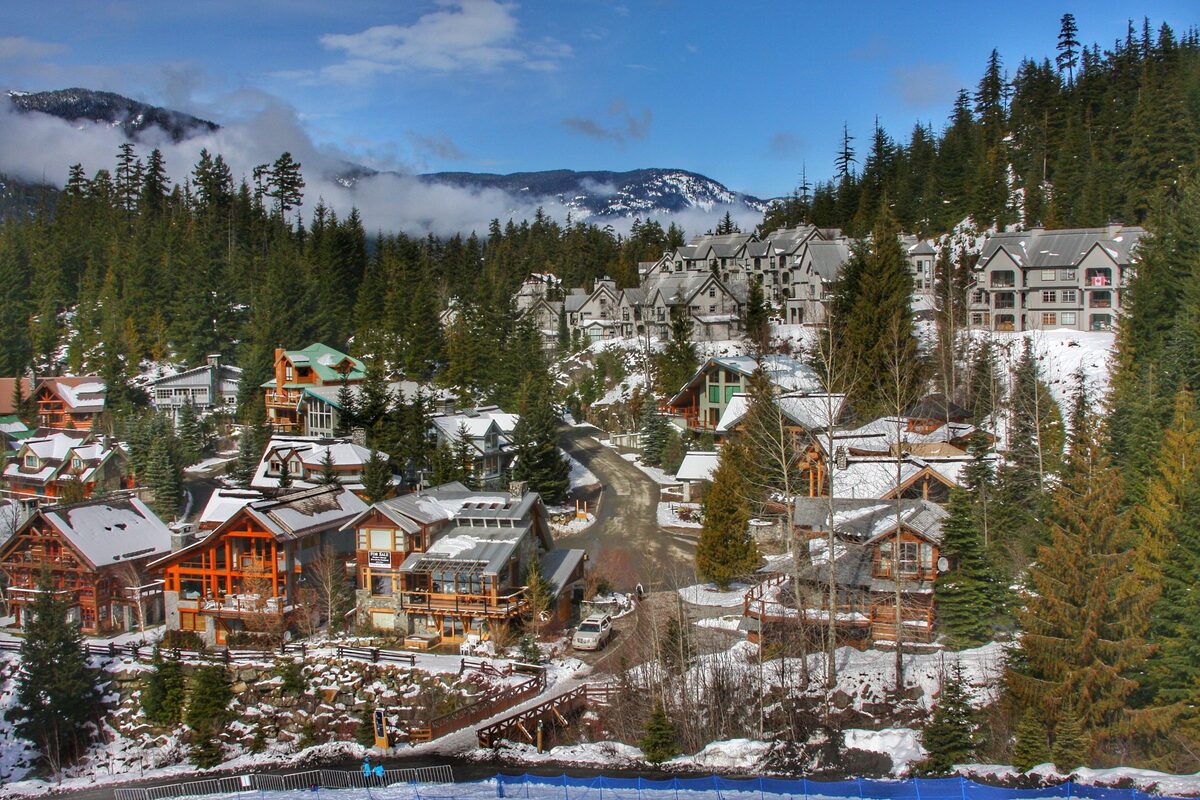 Chalets and lodges in the snow among evergreens in Whistler village, with mountains and cloud behind