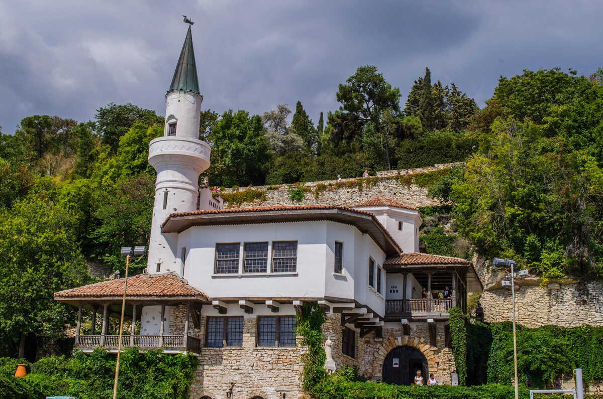 Queen Marie's white Balchik palace with its minaret-like tower and tiled roofs, set against a wooded, terraced hillside.