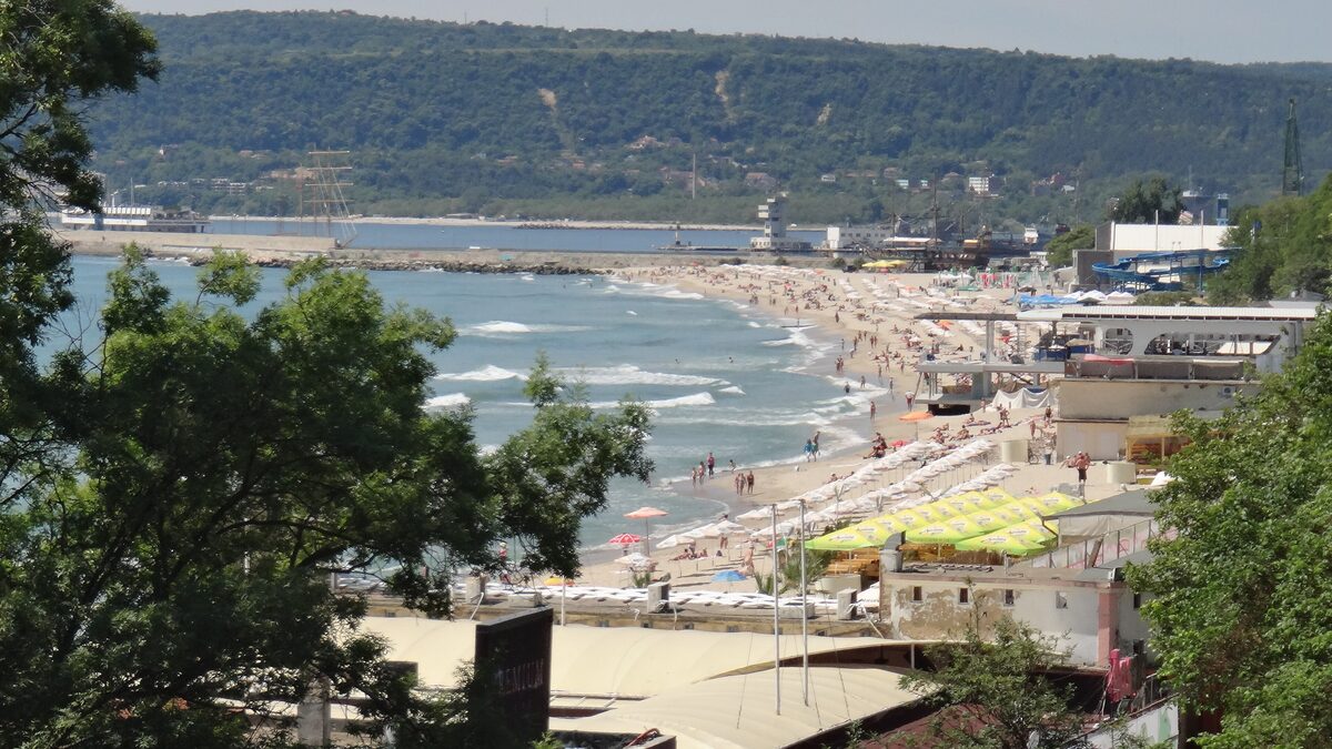 Varna's city beach seen from the Sea Garden above, with rows of parasols, beach bars and the port breakwater beyond.