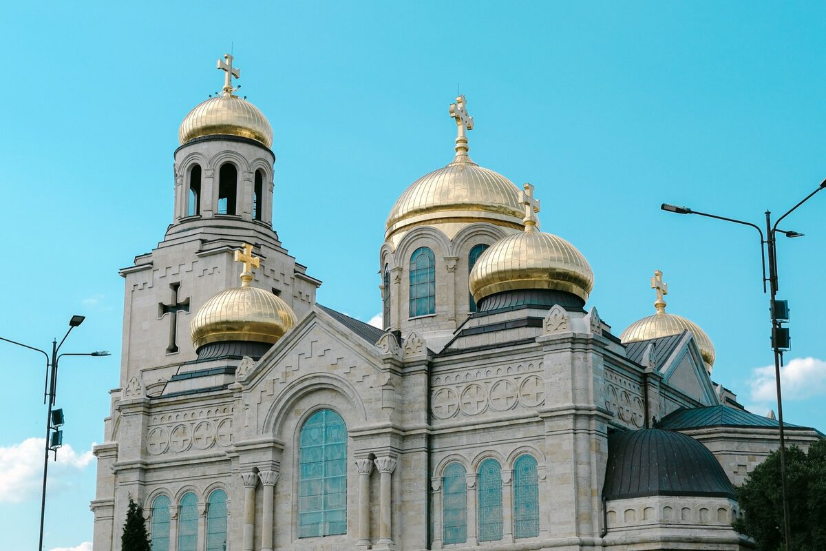 The bell tower and gilded onion domes of the Dormition Cathedral against a clear blue sky.