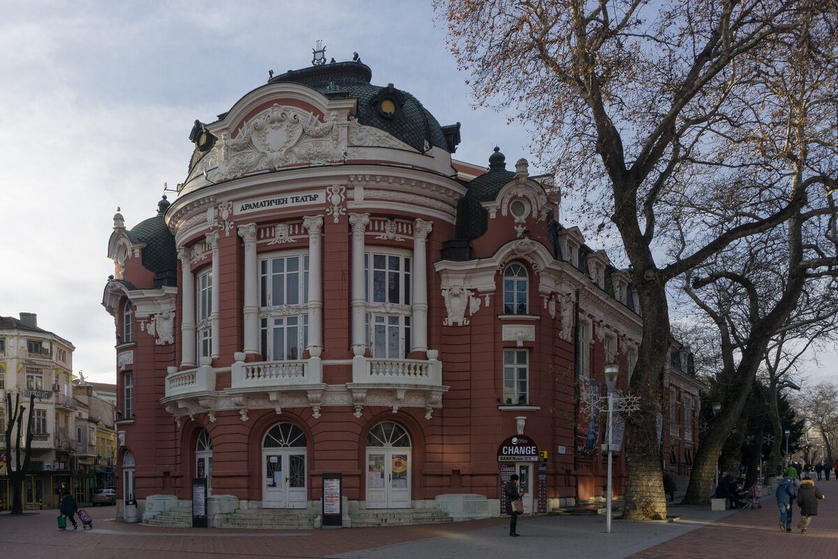 The red neo-Baroque Opera and Drama Theatre building on Independence Square, with plane trees along the pedestrian street.