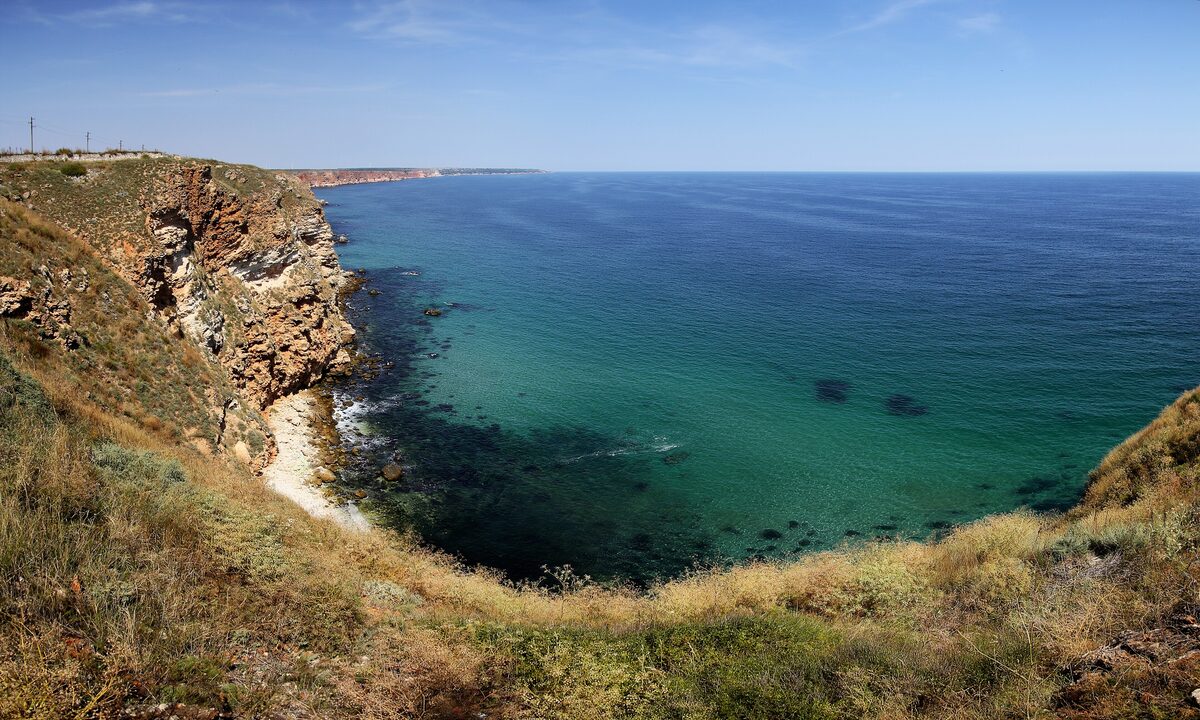 Red-brown cliffs at Cape Kaliakra falling into a clear turquoise bay of the Black Sea, looking north along the coast.