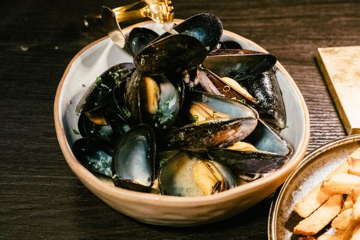 A bowl of steamed black mussels in a light herb broth, with a side of fries.