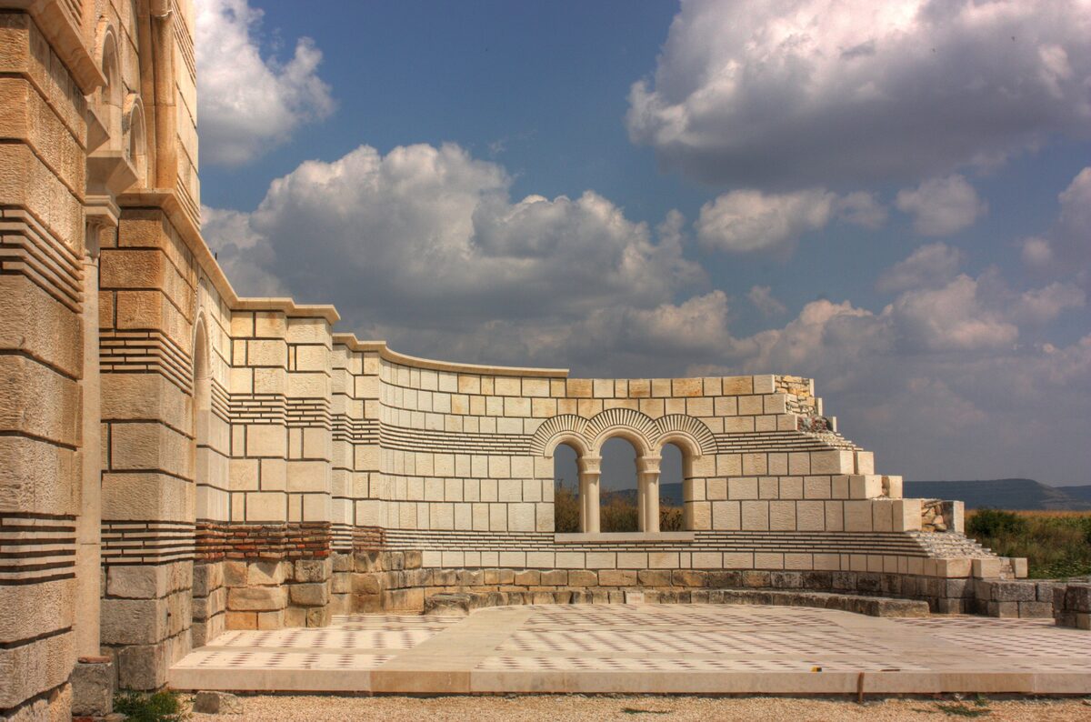 The partly rebuilt stone walls and arched triple window of the Great Basilica at Pliska under a cloudy sky.