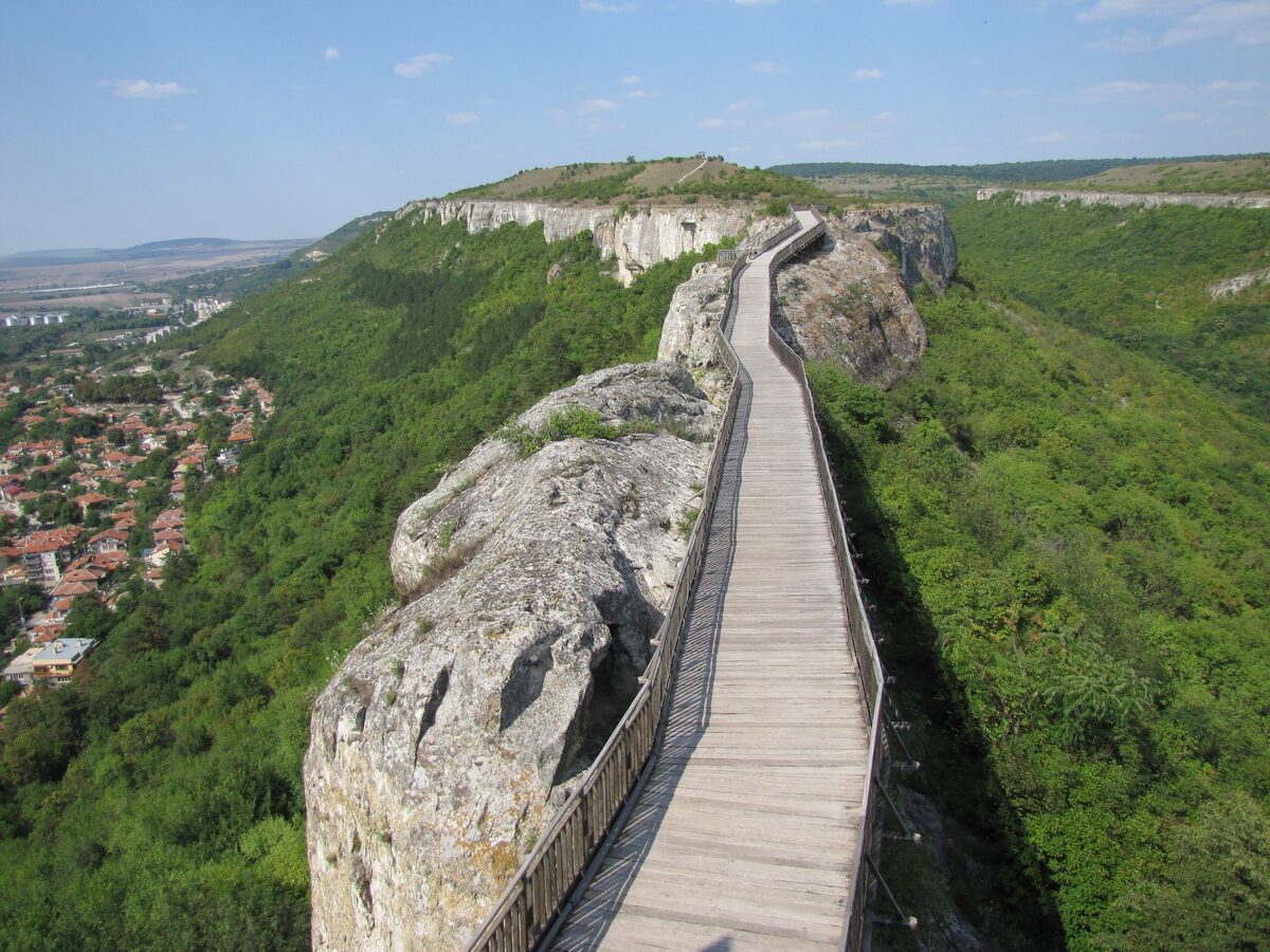 The long wooden footbridge to Ovech fortress running along a limestone ridge above the green valley and the rooftops of Provadia.