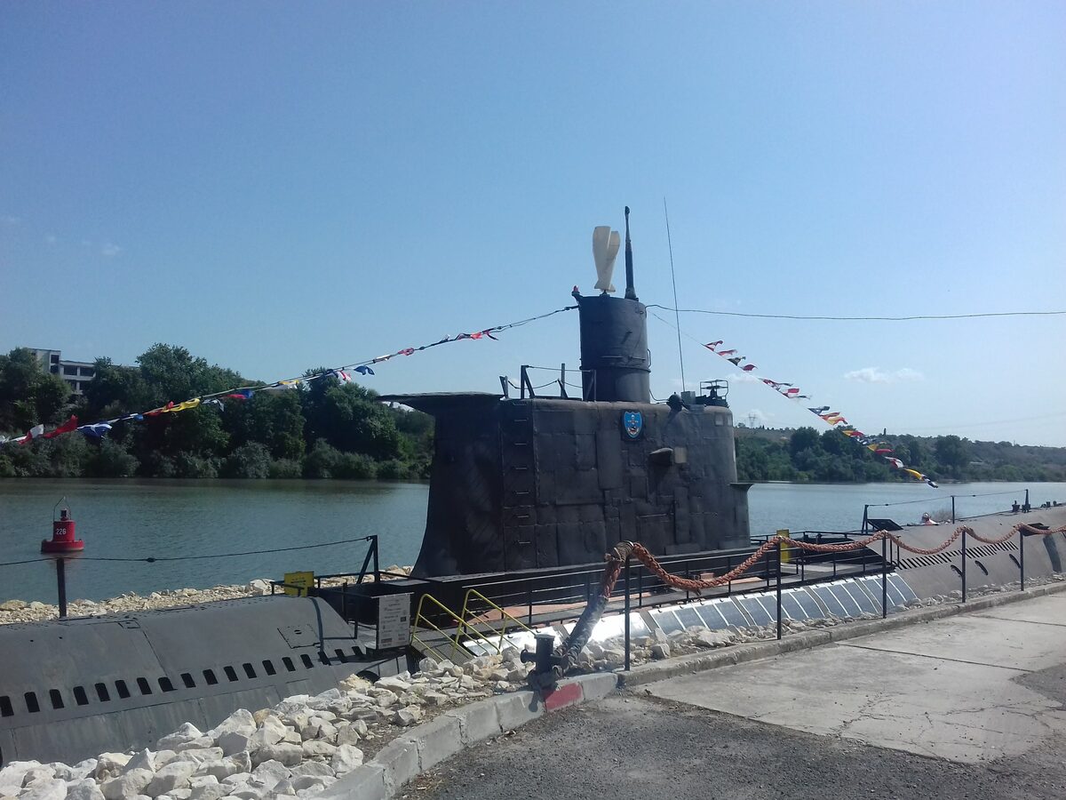 The black conning tower and hull of the submarine Slava moored as a museum on the Beloslav canal, strung with signal flags.
