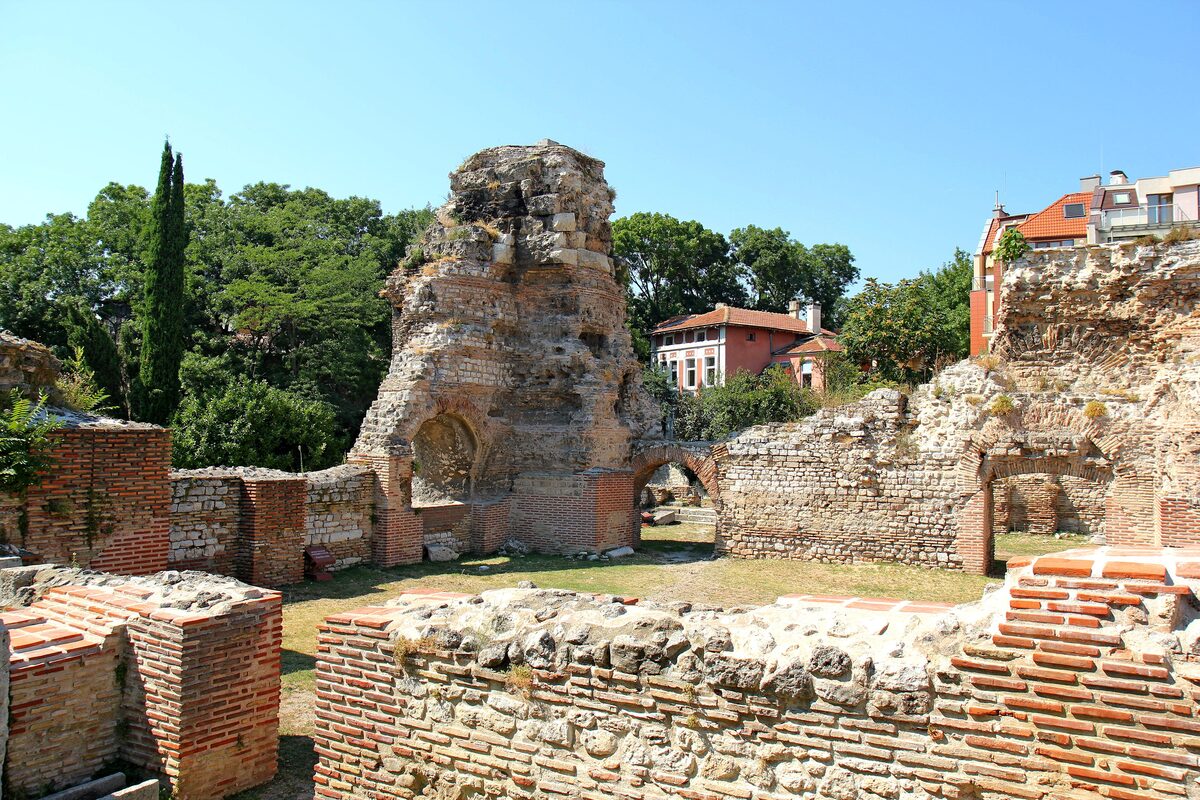 Brick and stone walls and a tall ruined arch of the Roman Thermae of Odessos under a clear summer sky.