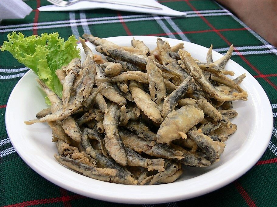 A plate of tsatsa, tiny sprats fried whole in a light batter, with a lettuce leaf on a checked tablecloth.