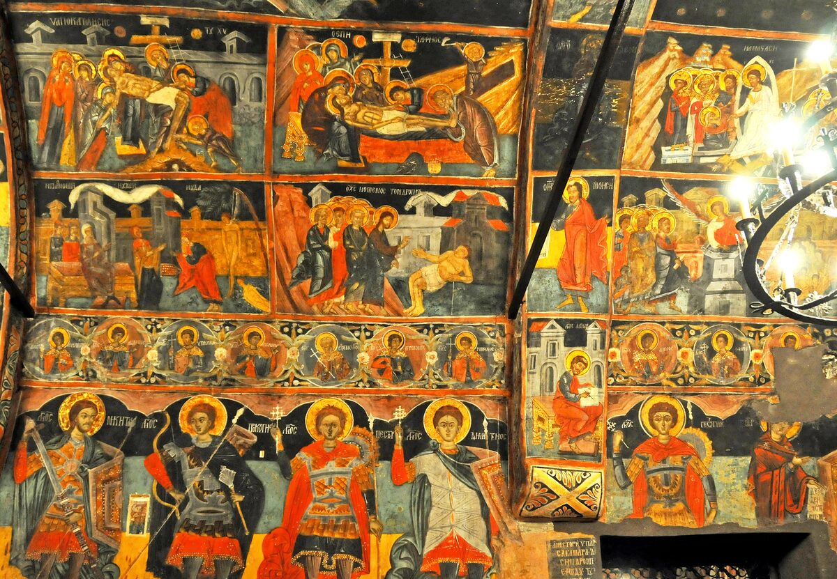 Seventeenth-century frescoes covering every inch of a wall and vault inside the Church of the Nativity in Arbanasi, with scenes from the life of Christ above rows of warrior saints.