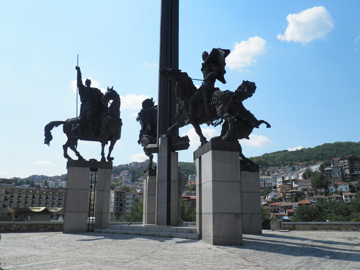 The bronze horsemen of the Asenevtsi monument around its central sword-shaped obelisk, with the hillside houses of Veliko Tarnovo behind.