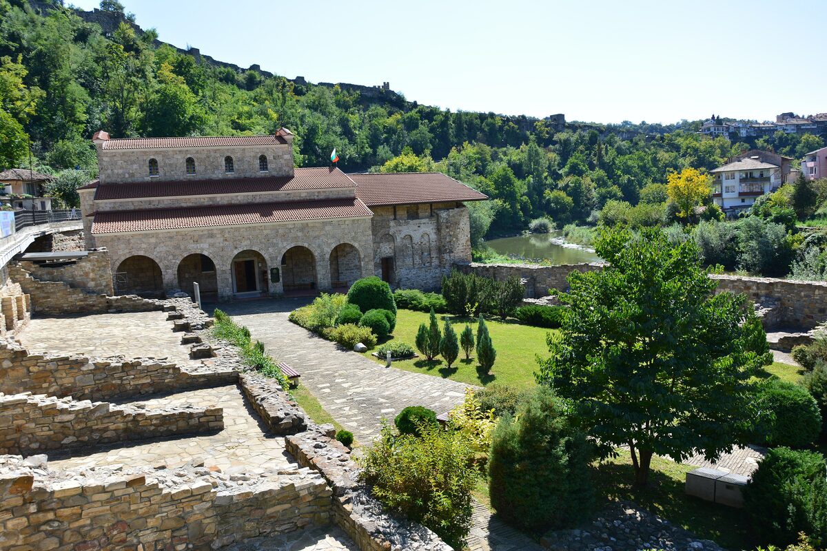 The arcaded stone Holy Forty Martyrs Church in Asenova mahala, with excavated foundations in front and the Yantra and Tsarevets' walls behind.